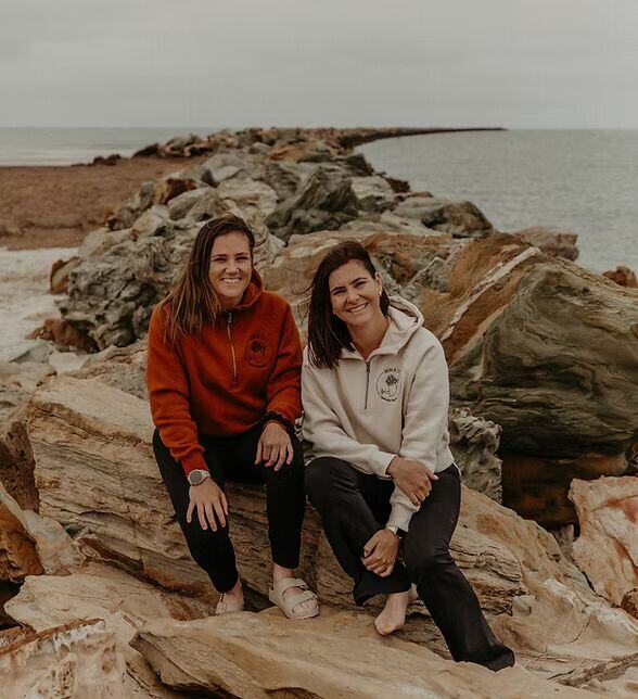 Ren and Em sitting together on rocks by the sea in South Australia